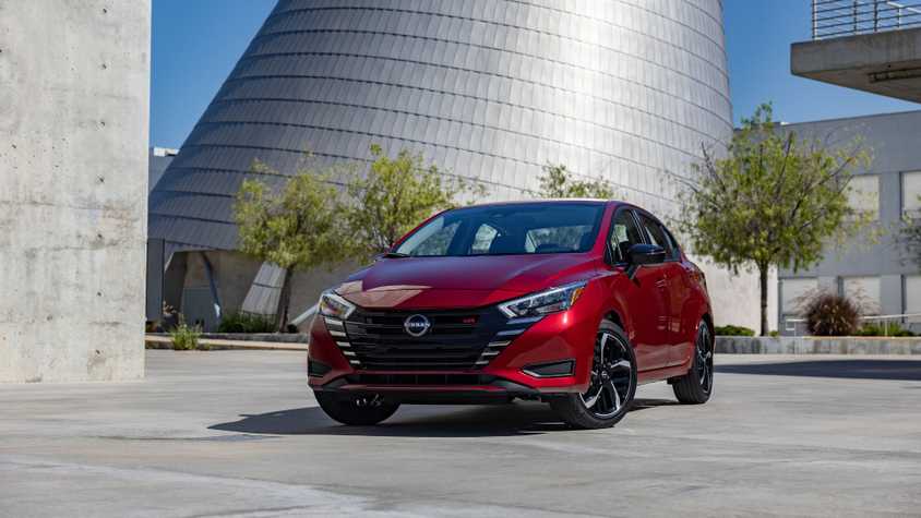 Front 3/4 view of a red 2025 Nissan Versa with a modern glass building in the background.