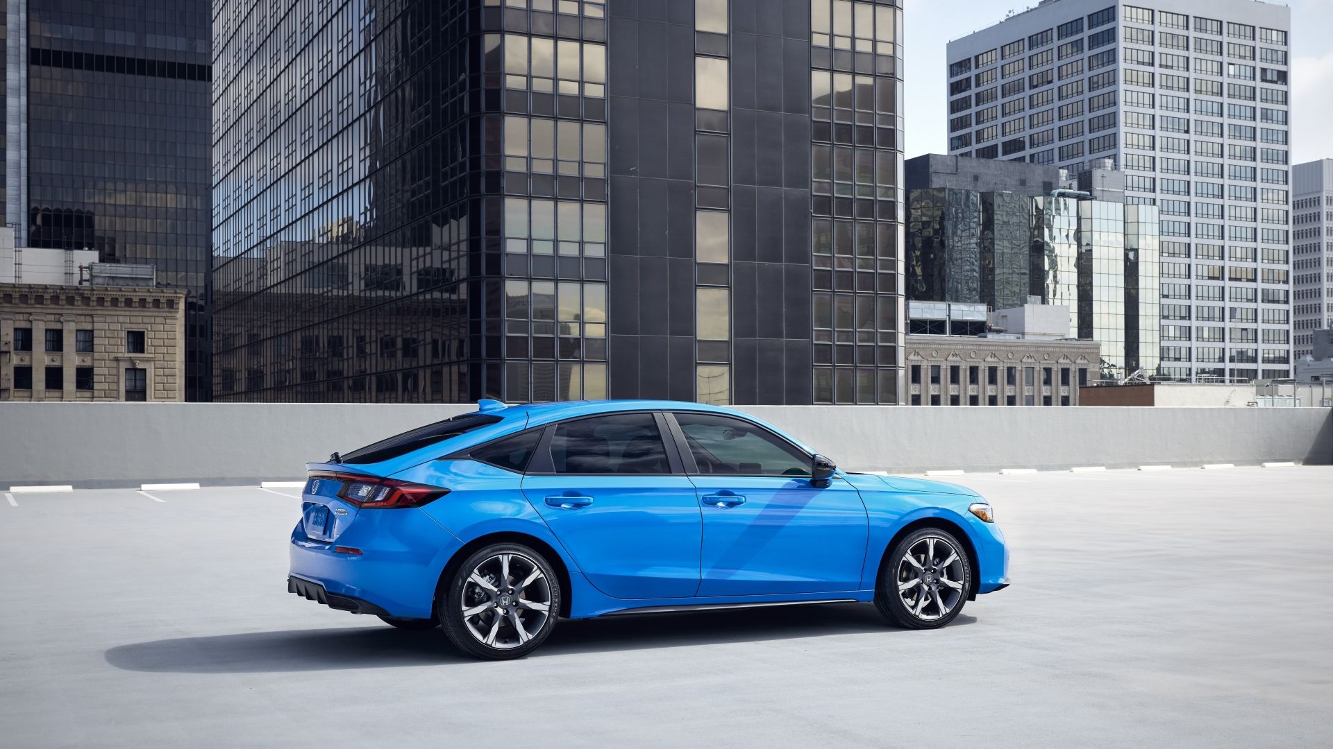 Side profile shot of a blue 2025 Honda Civic parked on a rooftop with tall buildings in the background.