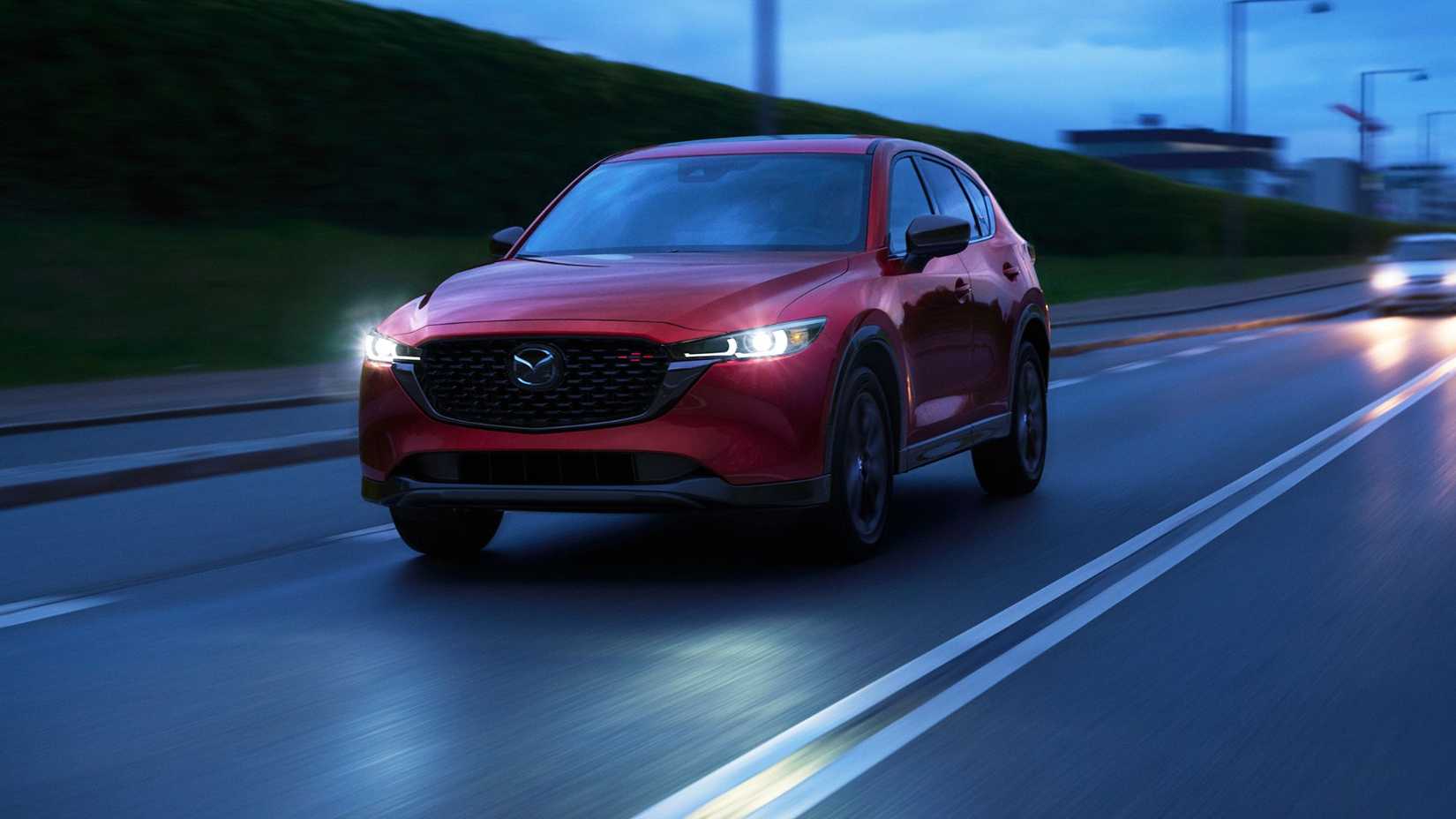 Front three-quarter view of a red 2025 Mazda CX-5 driving at night through a city.