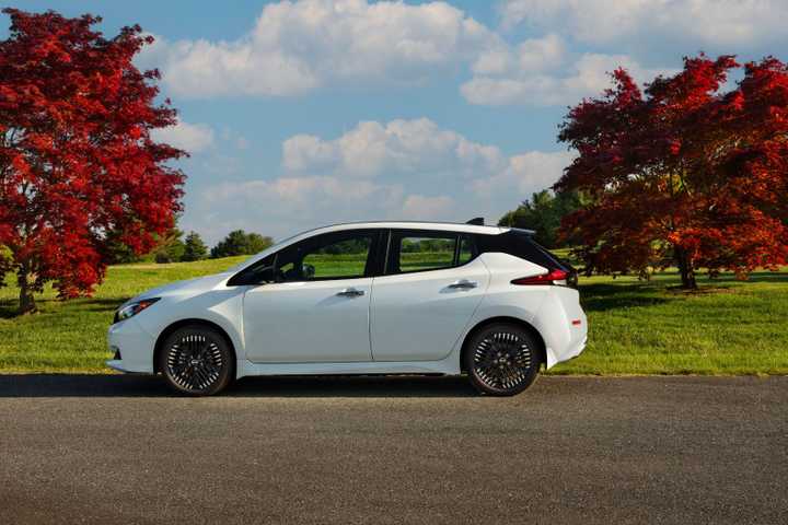 Static sider profile shot of a white 2025 Nissan Leaf with trees in the background.
