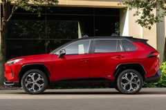 Static side profile shot of a red 2025 Toyota RAV4 PHEV XSE parked outside of a modern building.