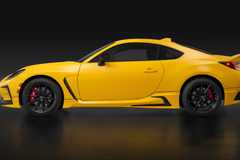 Side profile shot of a yellow 2026 Toyota GR86 Yuzu in a studio with a black backdrop.