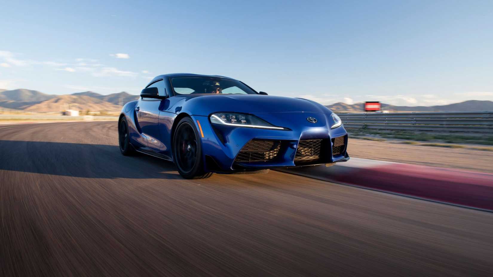 Front 3/4 view of a blue 2026 Toyota GR Supra driving around a racetrack.