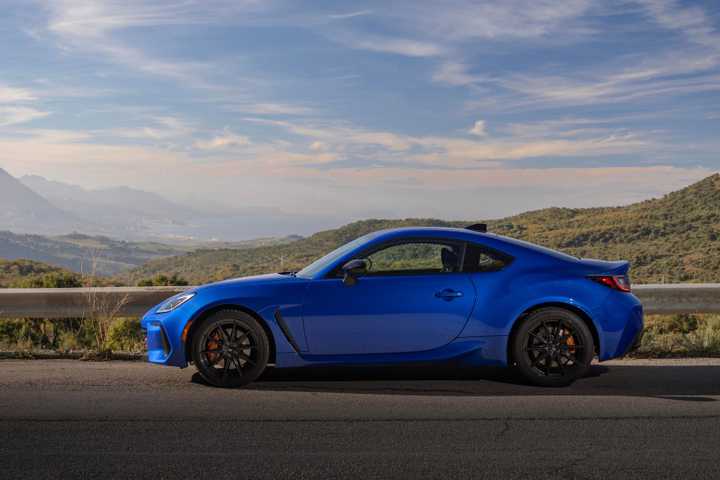 Static side profile shot of a blue 2024 Subaru BRZ tS with mountains and trees in the background.