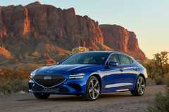 Front 3/4 shot of a blue 2025 Genesis G70 parked on gravel with a mountain in the background.