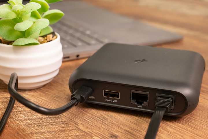A travel router next to a laptop and little plant. 