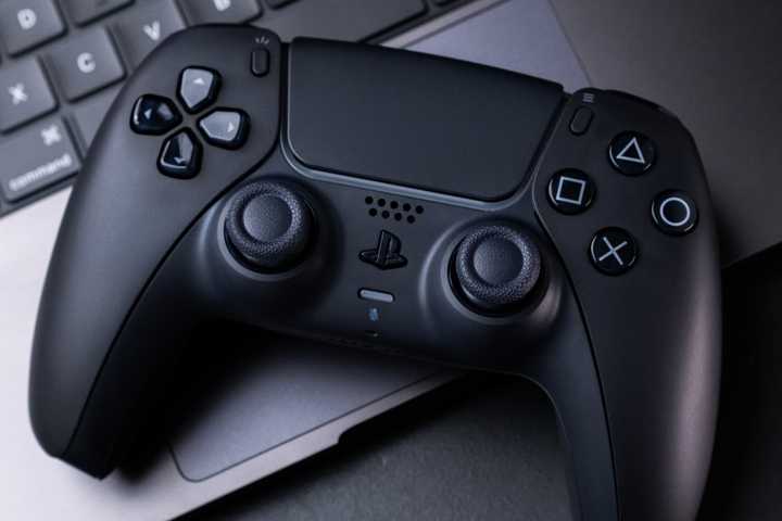 A black PlayStation 5 DualSense controller on a MacBook.