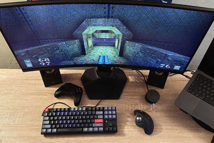 A desk with a gaming setup showing Quake on screen and a trackball mouse.