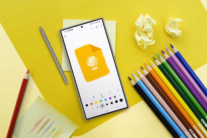 A desk with some colorful pencils and a phone in the center displaying a Google Keep sketch.