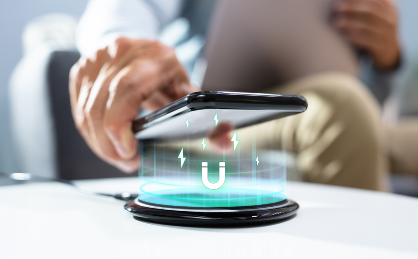 A hand lowers a smartphone onto a wireless charging pad, with glowing magnetic energy lines and a magnet icon projected between them.