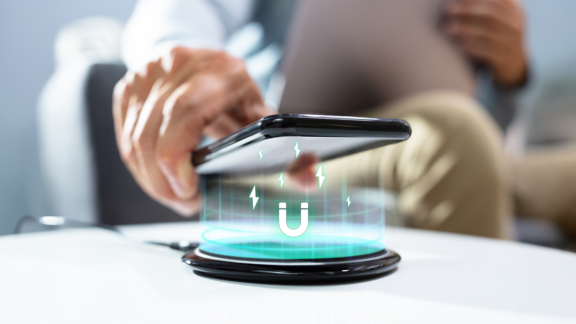 A hand lowers a smartphone onto a wireless charging pad, with glowing magnetic energy lines and a magnet icon projected between them.