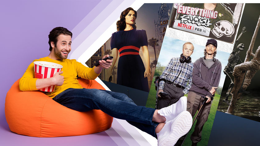 A man lounging on a beanbag, holding a TV remote and a bucket of popcorn, with TV show covers next to him.