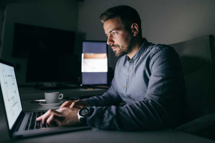 A man using a MacBook in a dark room at night.