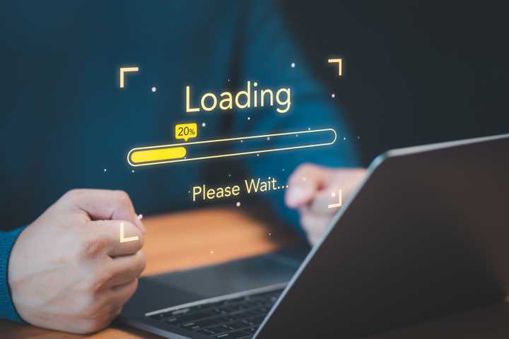 A person using a laptop with fists clinched in frustrating and a loading progress bar floating above the laptop.