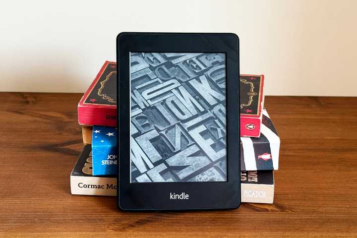 A stack of paper books with a Kindle eReader in front of them.