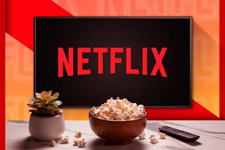 A TV with the Netflix logo with a plant a popcorn bowl and a remote control on a table.