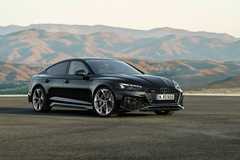 Full view of a black Audi RS5 Sportback parked on tarmac with mountains in the background.
