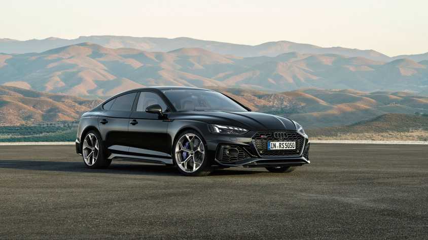 Full view of a black Audi RS5 Sportback parked on tarmac with mountains in the background.