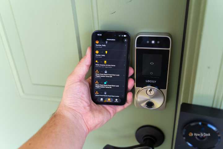 An iPhone with the Apple Home app opened showing automations being held next to a Lockly Visage smart lock.
