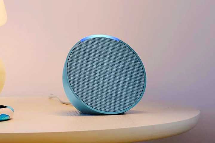 An Echo Pop on a table next to a lamp