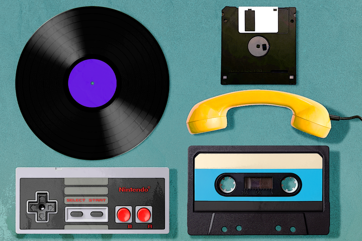 Flat lay of vintage tech items on a teal surface, including a vinyl record, floppy disk, yellow telephone handset, cassette tape, and a Nintendo controller.