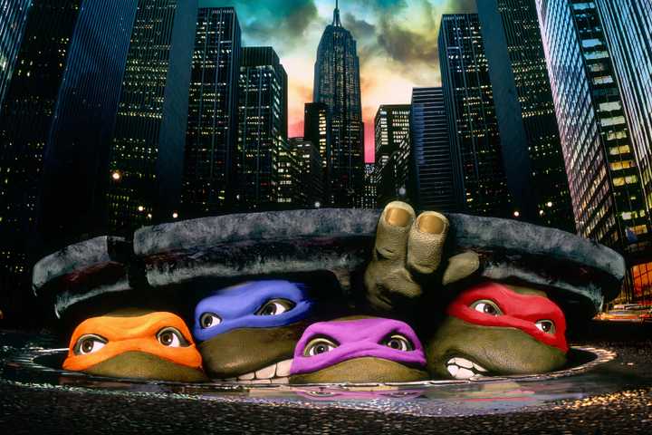 Four teenage mutant ninja turtles under a sewer cover with a city in the background