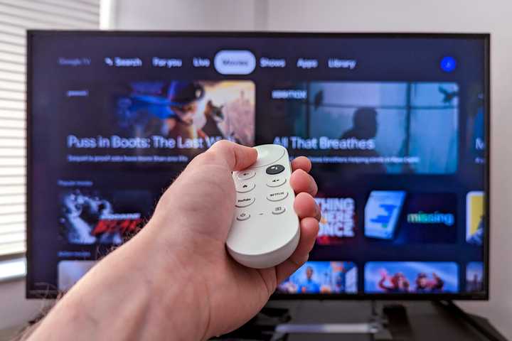 Person holding a Chromecast remote infront of a tv with Google TV open.