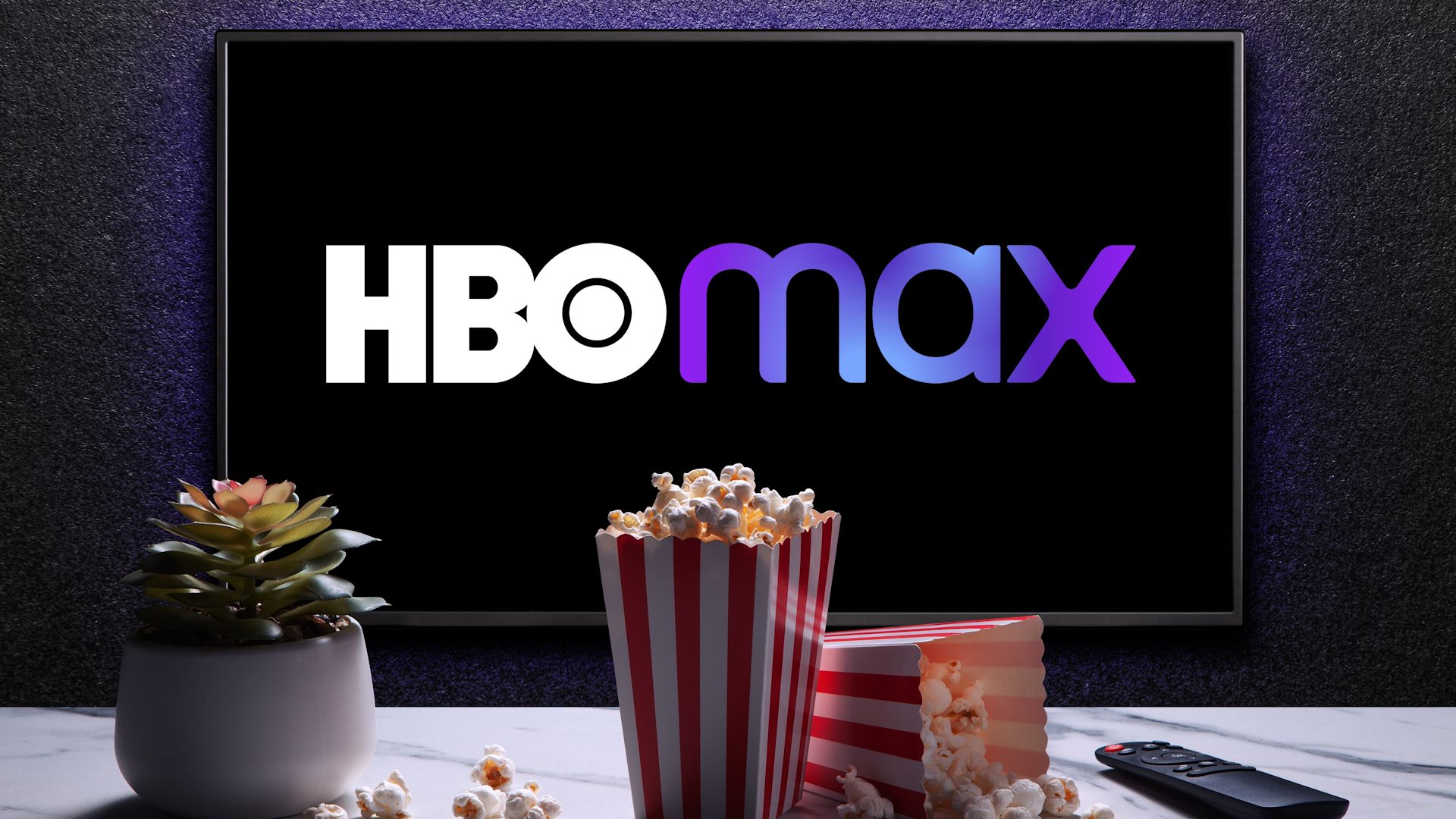 HBO Max logo on TV with popcorn boxes, remote control and home plant on the table.