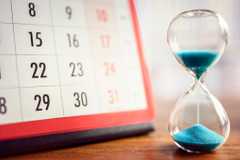 An hourglass on a tabletop next to a calendar.