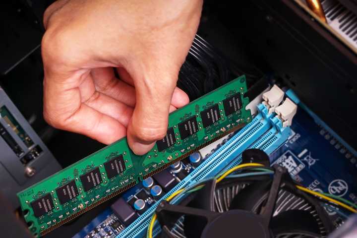 A persons hand pushing a stick of RAM into place inside a desktop PC.