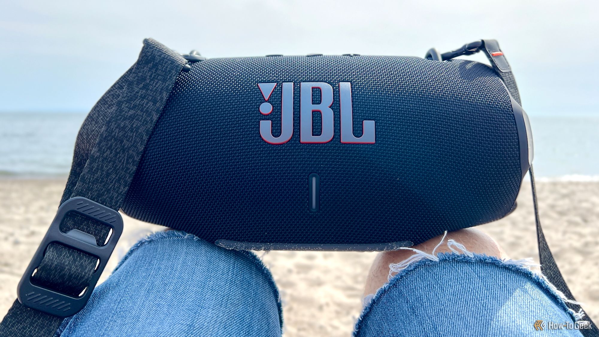 The JBL Xtreme 4 Bluetooth speaker resting on someone's knees at the beach.