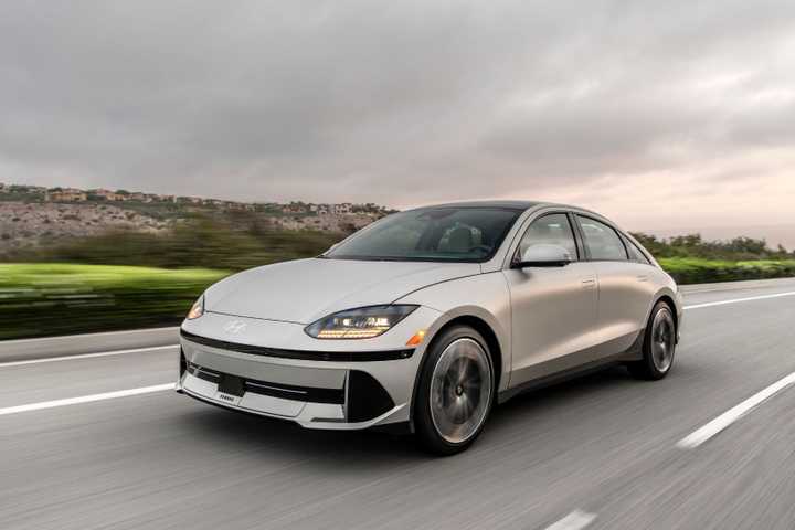 Dynamic front 3/4 shot of a silver 2025 Hyundai Ioniq 6 driving on a country road.