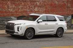 Front three-quarter view of a white 2025 Hyundai Palisade parked alongside a sidewalk with a brick wall with graffiti on it.