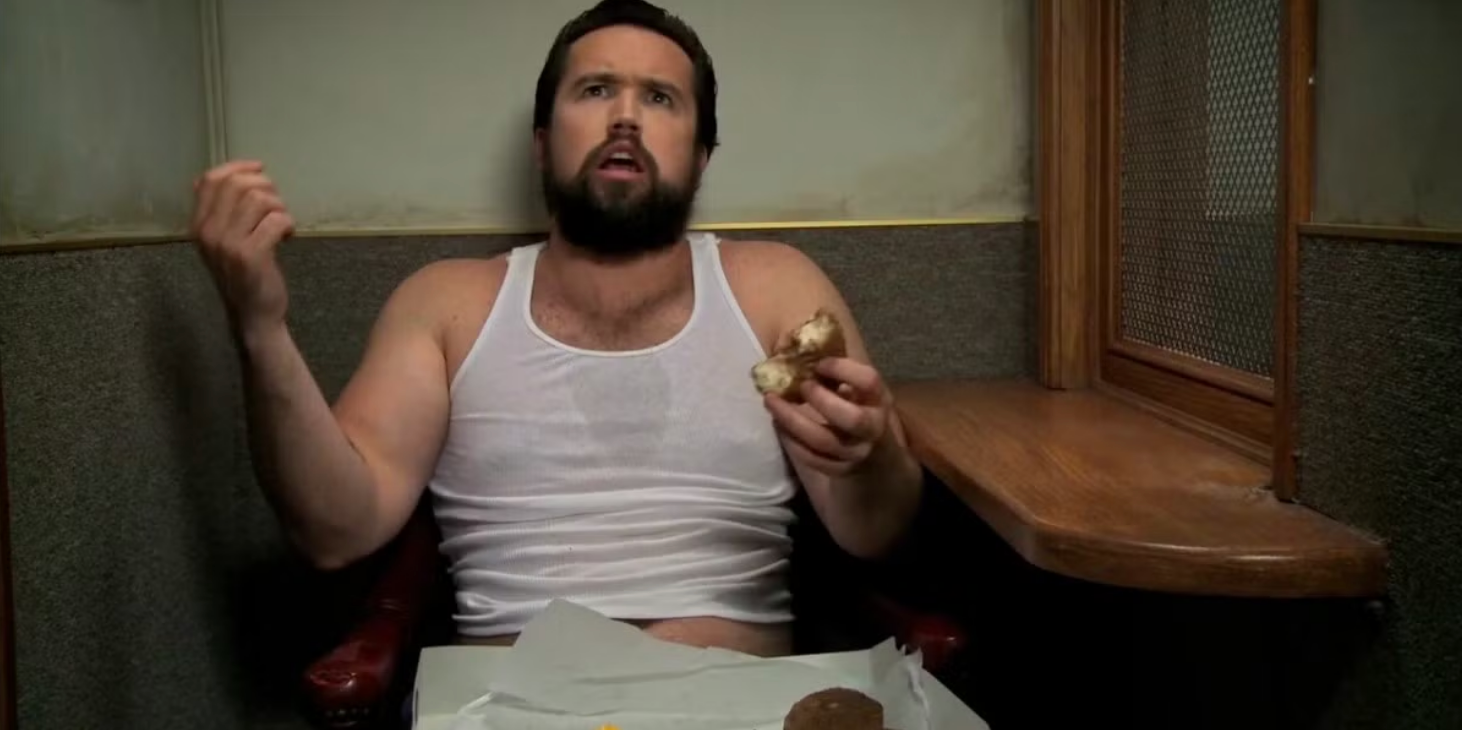 Rob McElhenney as Mac, eating food while confessing to a priest in It's Always Sunny in Philadelphia.