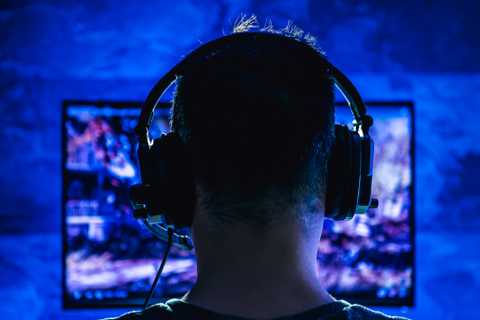 Back of a man's head as he's gaming late at night with wired headphones on.