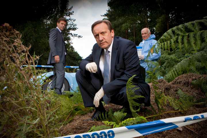 Midsomer Murders three cast members kneeling to observe a crime scene.