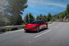 Front 3/4 shot of a red 2024 Tesla Model 3 driving on a winding country road.