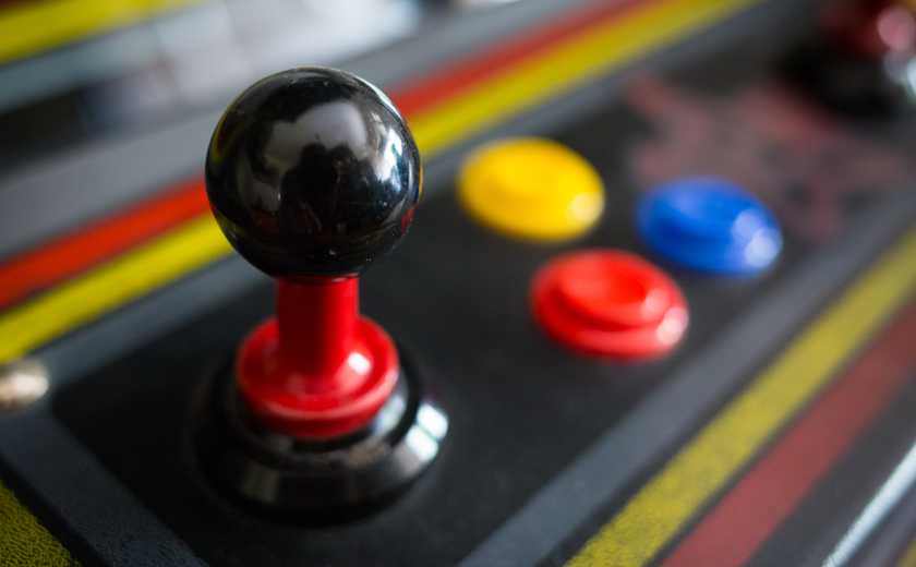 A close up view of a standup arcade machine's joystick and its three buttons. 