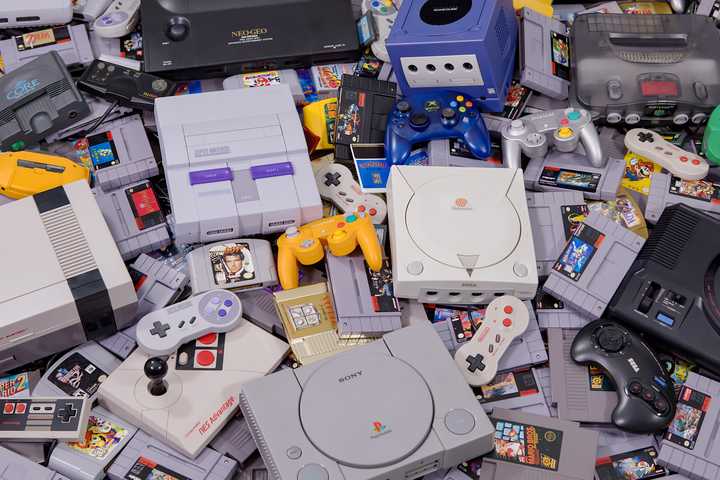 A pile of different gaming systems, along with random game controllers and gaming cartridges.