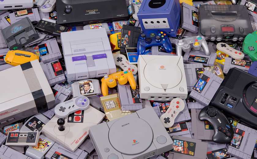 A pile of different gaming systems, along with random game controllers and gaming cartridges.