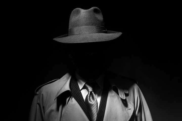 Shadowy detective figure in a hat, suit, and jacket.