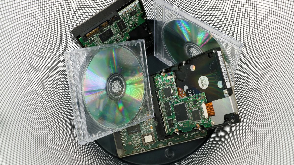 Old compact discs and computer hardware discarded in a trash bin.