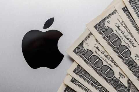 Close-up of Apple company sign and fan of dollar bills on the cover of the MacBook.