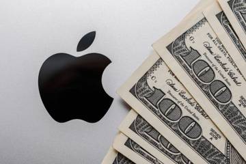Close-up of Apple company sign and fan of dollar bills on the cover of the MacBook.