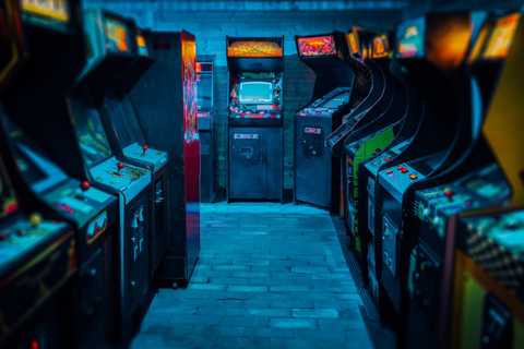 Old Vintage Arcade Video Games in an empty dark gaming room with blue light with glowing displays and beautiful retro design.