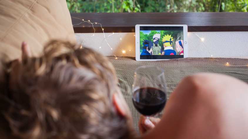 A person drinking wine in bed while watching Naruto.