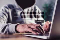 A dark hooded figure ominously using a laptop. 