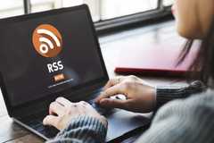 A woman sits in front of a laptop showing the RSS logo.