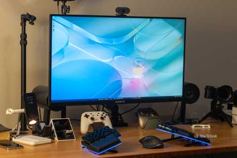 A GIGABYTE M32U 16:9 4K gaming monitor on a desk with a keyboard, controllers, and other accessories.