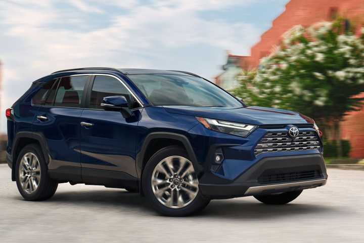 Dynamic front 3/4 shot of a blue 2025 Toyota RAV4 driving in a city.